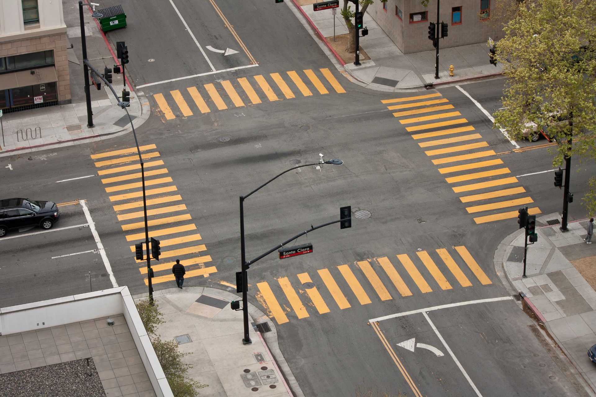 Aerial view of an urban intersection with bright yellow crosswalks. A lone pedestrian walks, while minimal traffic suggests a quiet city scene.
