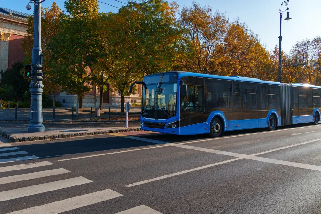 Blue city bus waits at crosswalk in city traffic.