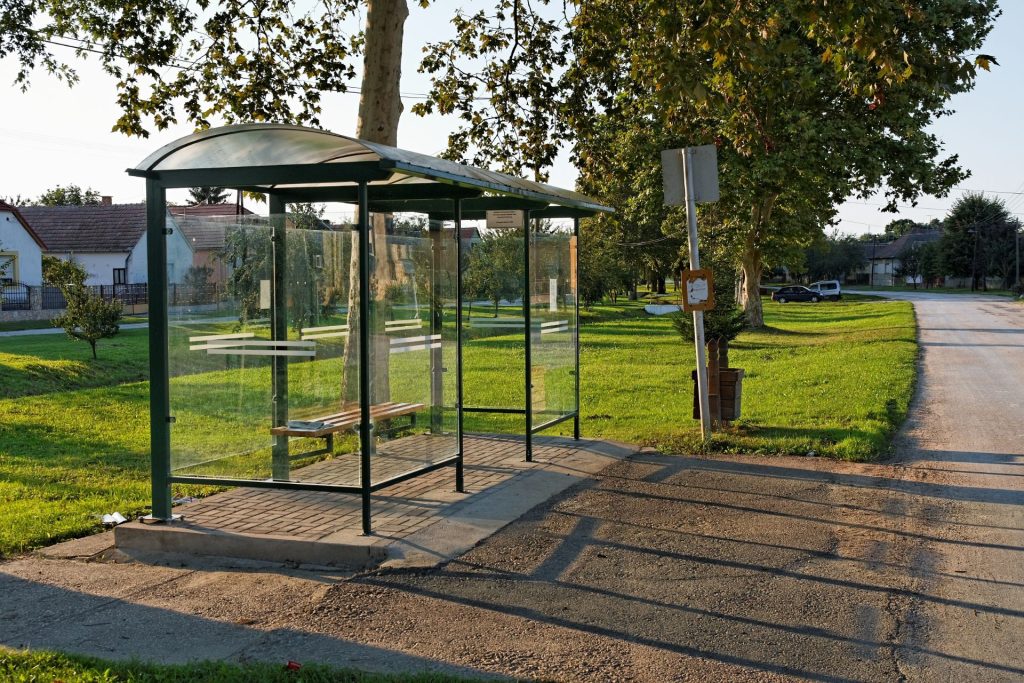 Enclosed bus shelter in grassy area off side of the road.