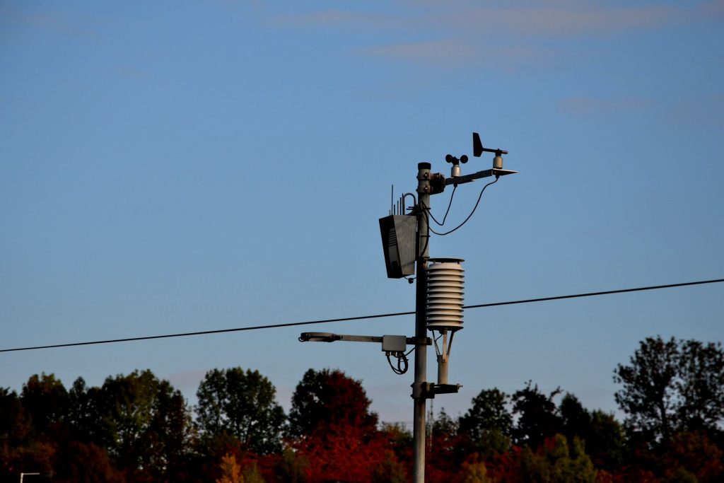 Weather sensing equipment attached to power line in treelined landscape.